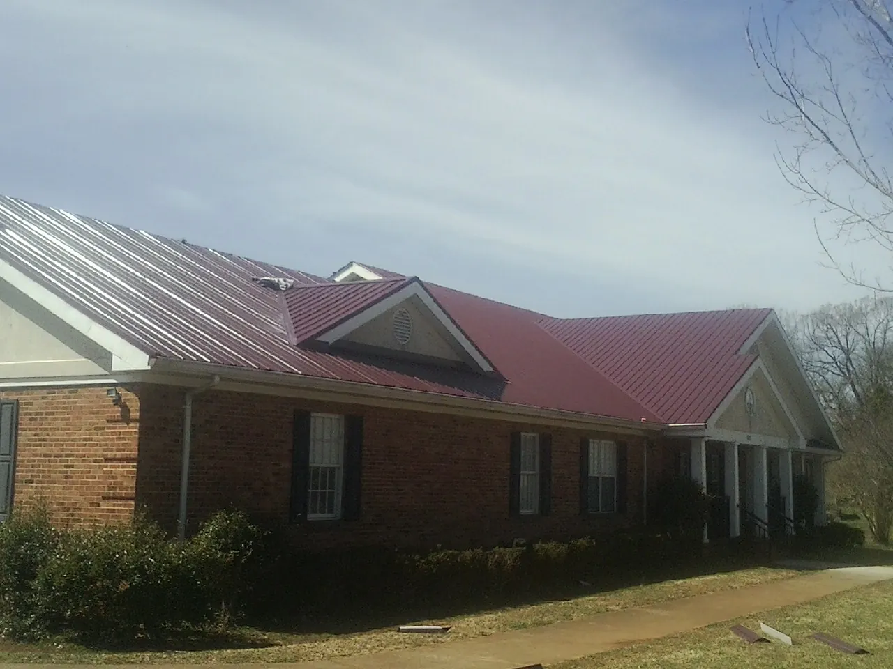 Red metal roof with gabled entries on a long brick building, from a Hail Damage Roof Repair job in New Prague