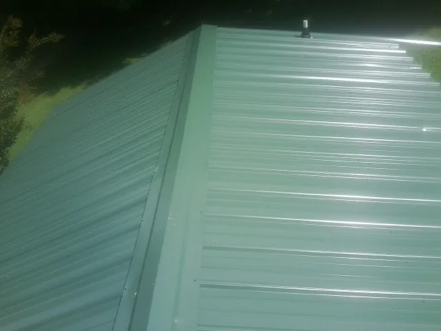 New green metal panels meeting at the ridge of a roof — Flat Roof Repair work by our crew in New Prague