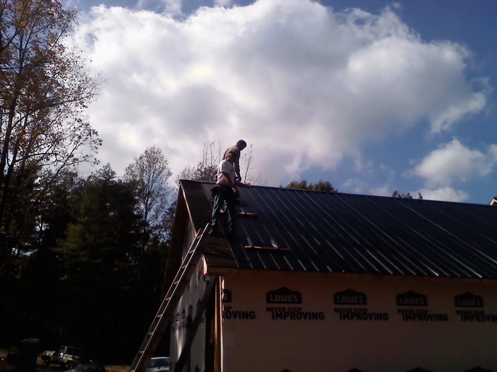 Roofer fastening dark metal panels high against a cloudy sky, from a Roof Inspection job in New Prague