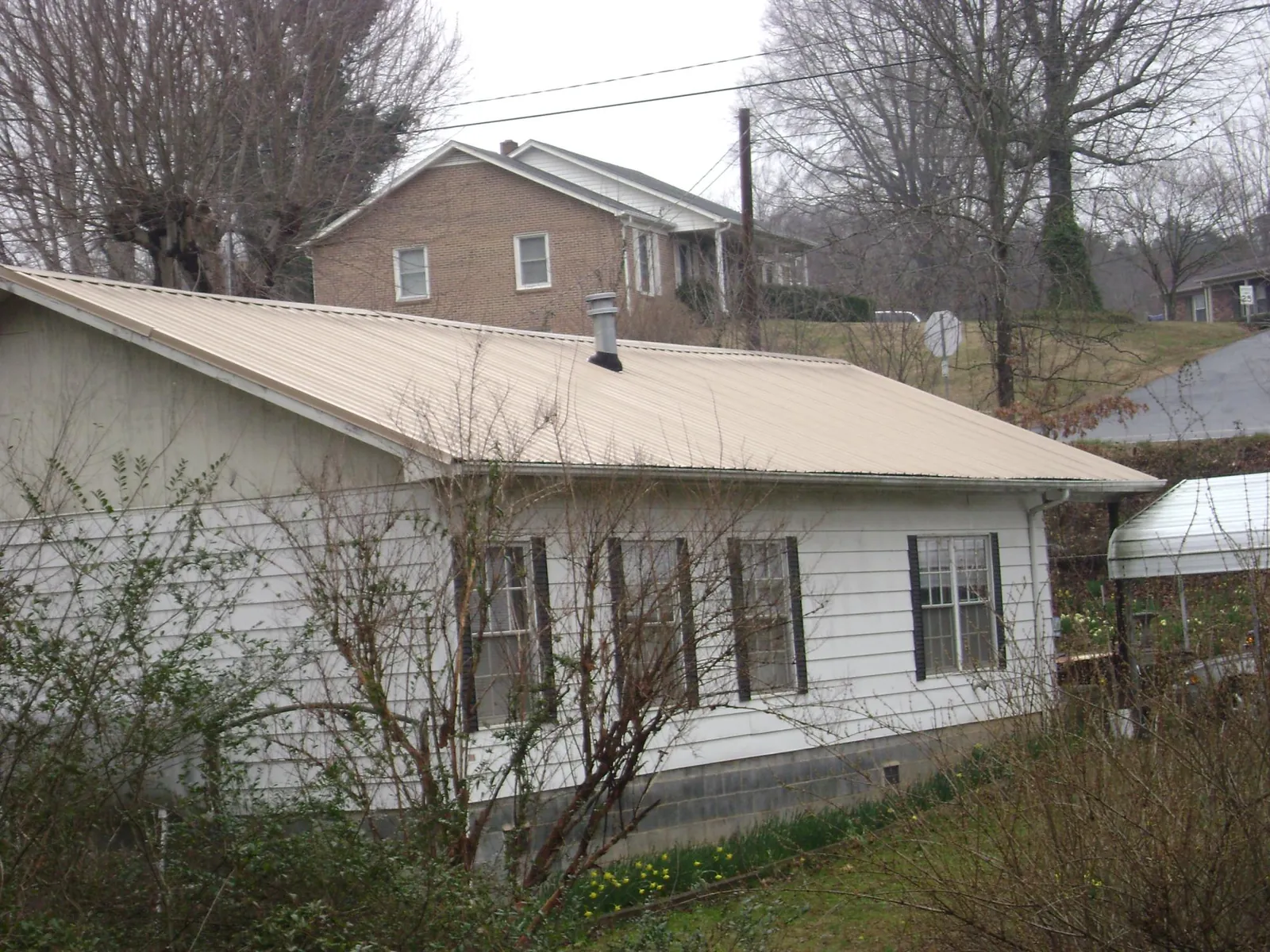 Tan metal roof on a white sided house set into a hillside — Commercial Roofing by Roofing Brothers in New Prague